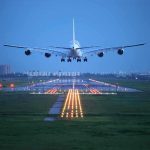 An airplane approaching the runway at night with landing lights illuminated