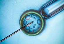 Close up of a needle and vial with liquid droplets on a blue background