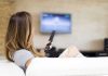 A woman sitting on a sofa holding a remote control and watching television