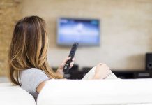 A woman sitting on a sofa holding a remote control and watching television