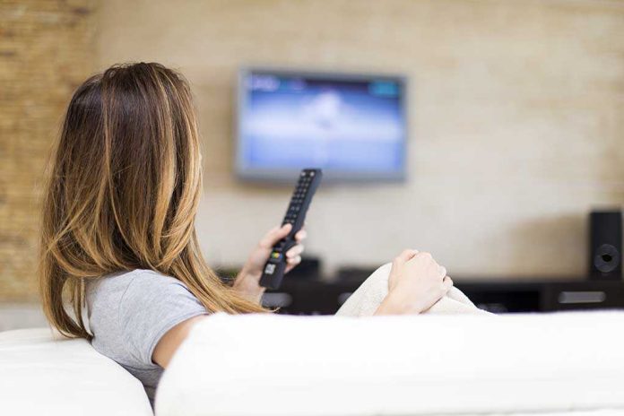 A woman sitting on a sofa holding a remote control and watching television