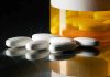 White pills beside an orange pill bottle.
