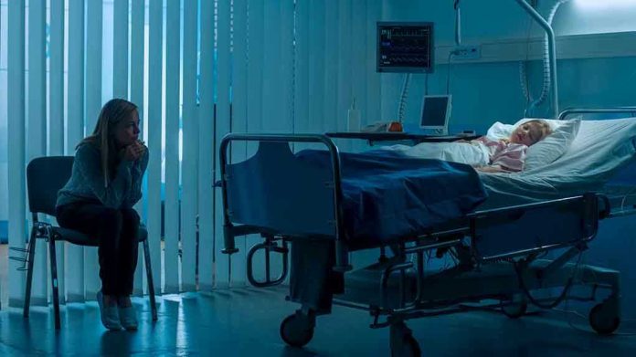 1181842819 Woman sitting beside hospital bed at night.