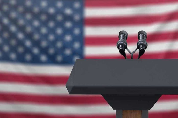 1223942518 Podium with microphones in front of American flag.