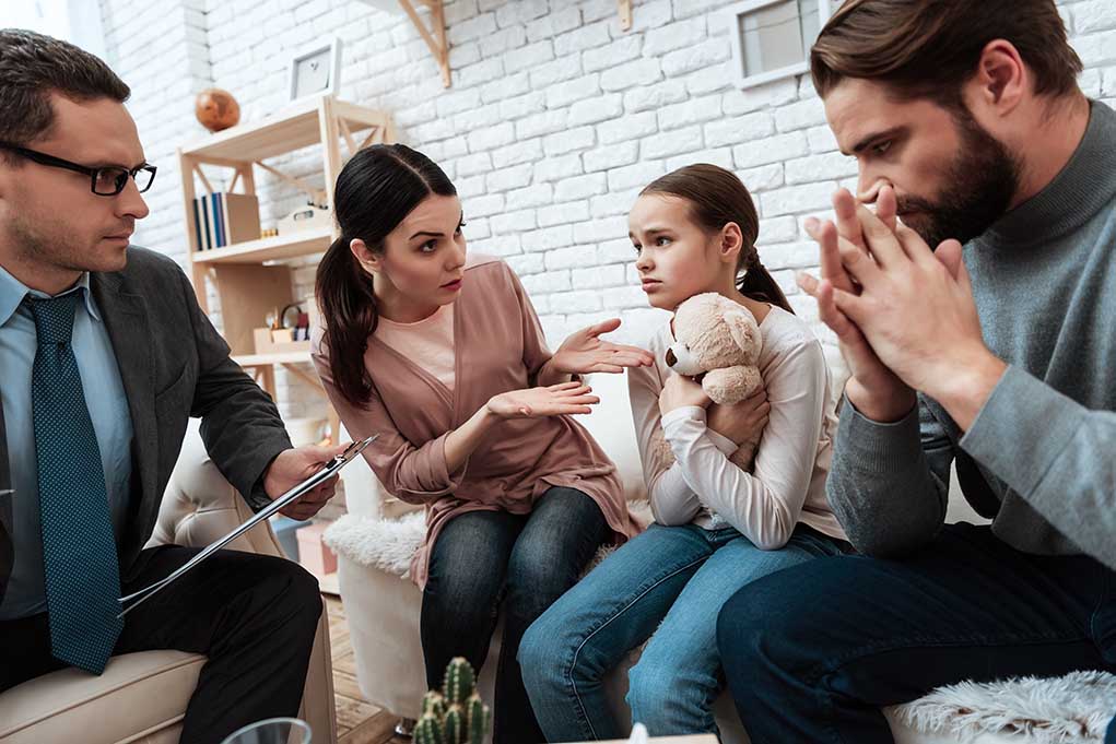 Family discussing with therapist, young girl holding teddy.