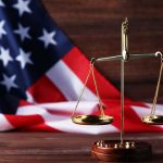 Attorneys Explore Presidential Pardons’ Influence On Capitol Riot Cases Scales of justice and American flag background.