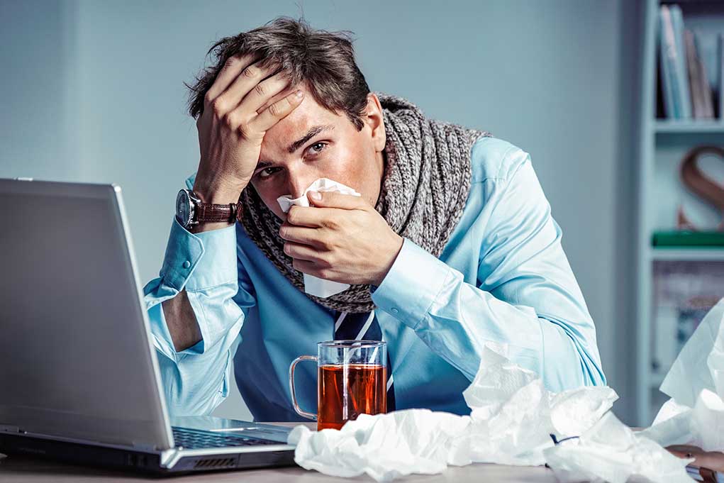 Sick person with laptop and tissues at desk