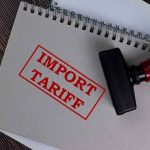 How Will New Tariffs Affect U.S. Computer Prices By 2025? Notebook with "Import Tariff" stamp and rubber stamper.