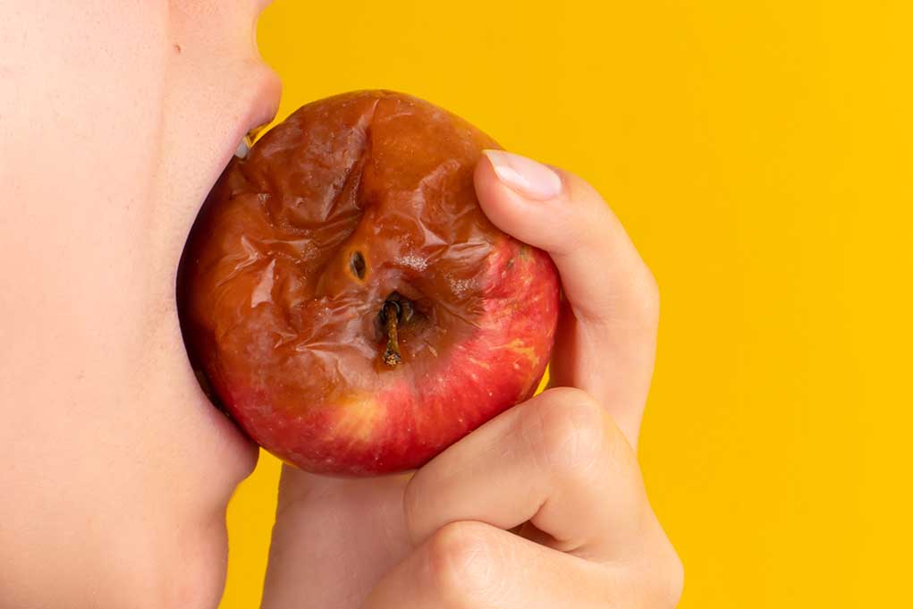 Person biting a rotten apple with yellow background