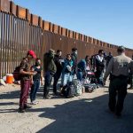 Group of people at border wall with patrol agents.