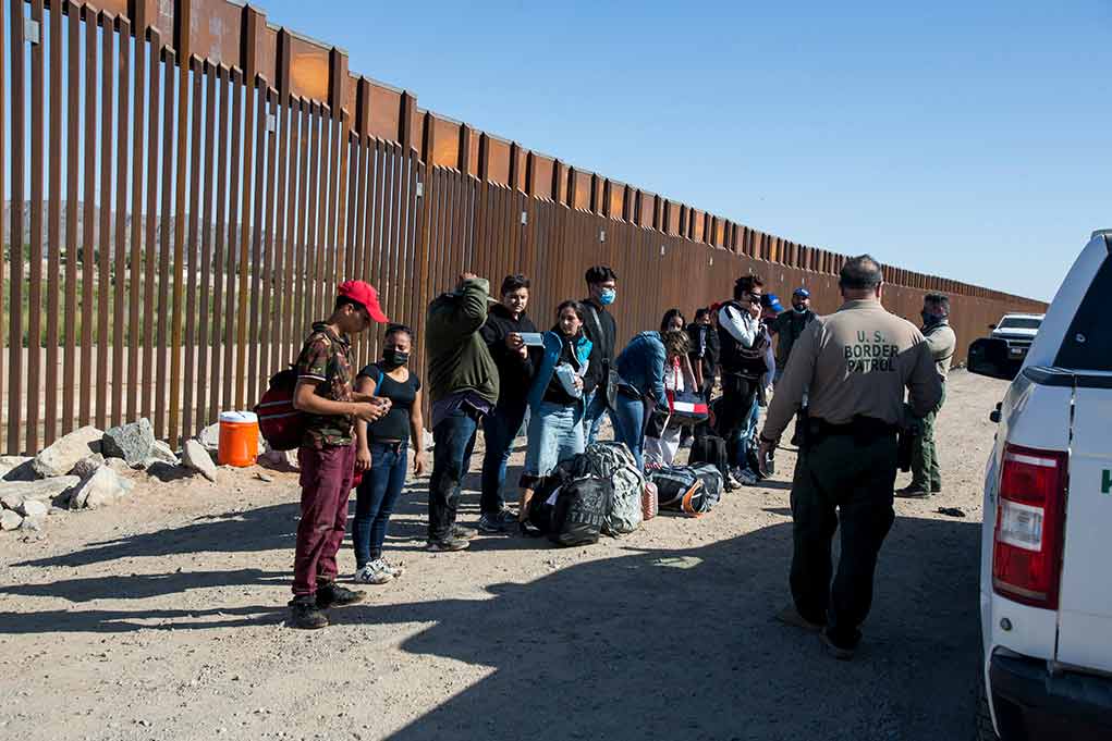 Group of people at border wall with patrol agents.