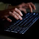 Why Monitoring The Dark Web Is Crucial For Cybersecurity Strategies Hands typing on a backlit keyboard in darkness