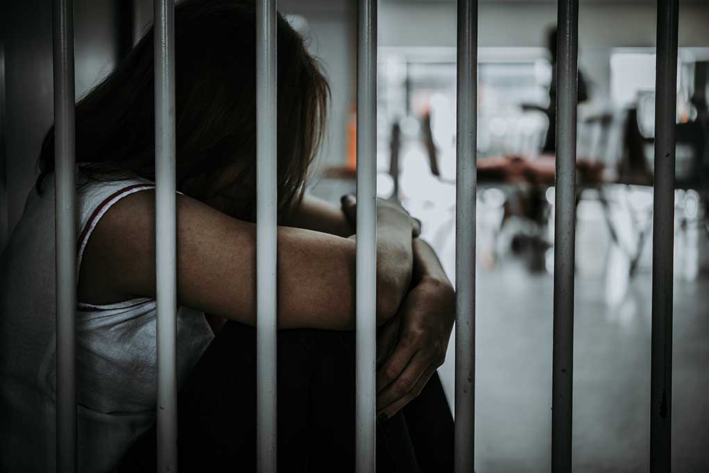 Person sitting behind bars in a dimly lit room