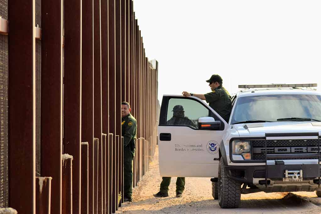 1545833798 featured image Border patrol agents near a tall metal fence.
