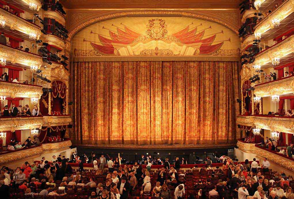 1413369908 featured image Ornate theater, grand curtain, audience seated below balconies.
