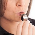 Whistleblower Family’s Lawsuit Sparks Debate On Aerospace Accountability Person blowing a silver whistle close-up.