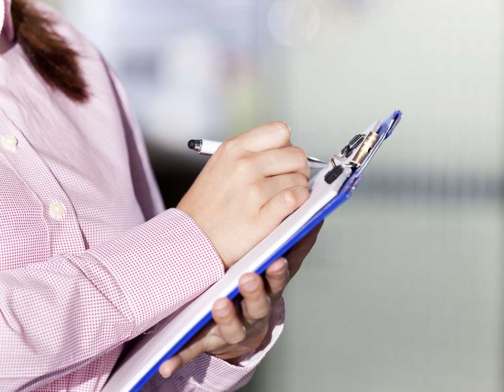 376166491 featured image a supervisor in a pink jacket makes marks on a clipboard with a pen.