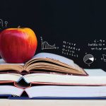 Linda McMahon Wants To Empower Choice In Education an apple sits on top of several open books with a chalkboard in the background