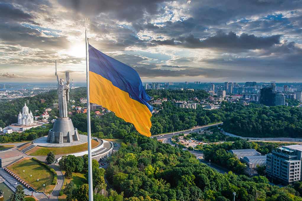 Ukrainian flag flying near city with statue monument