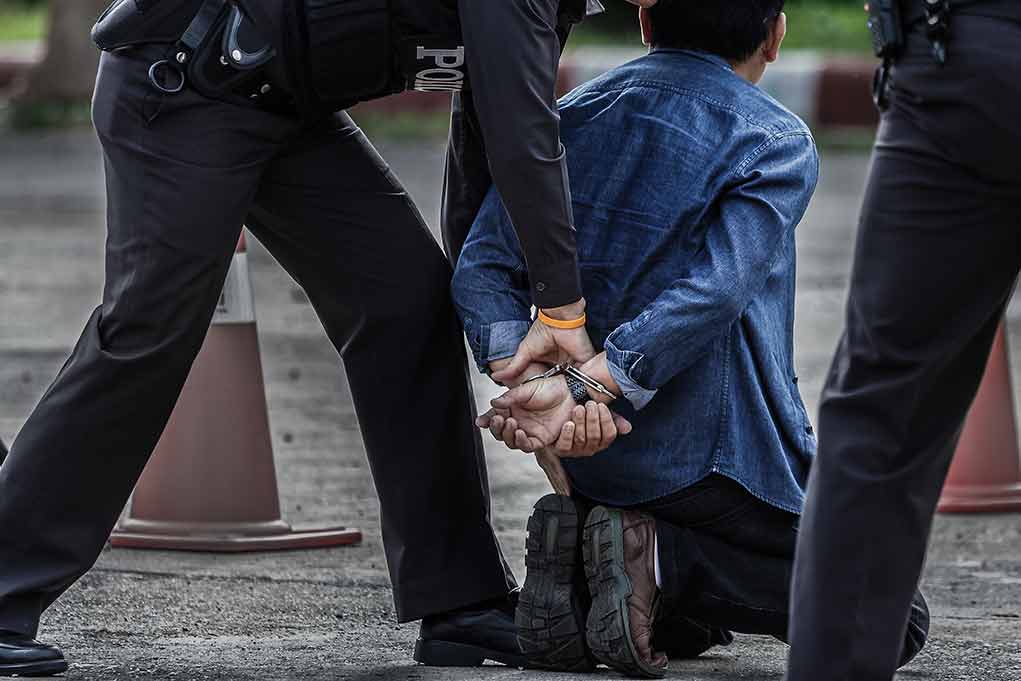 659470504 featured image Person kneeling handcuffed by police officers outside