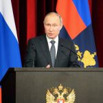 Man speaking at podium with flags behind him