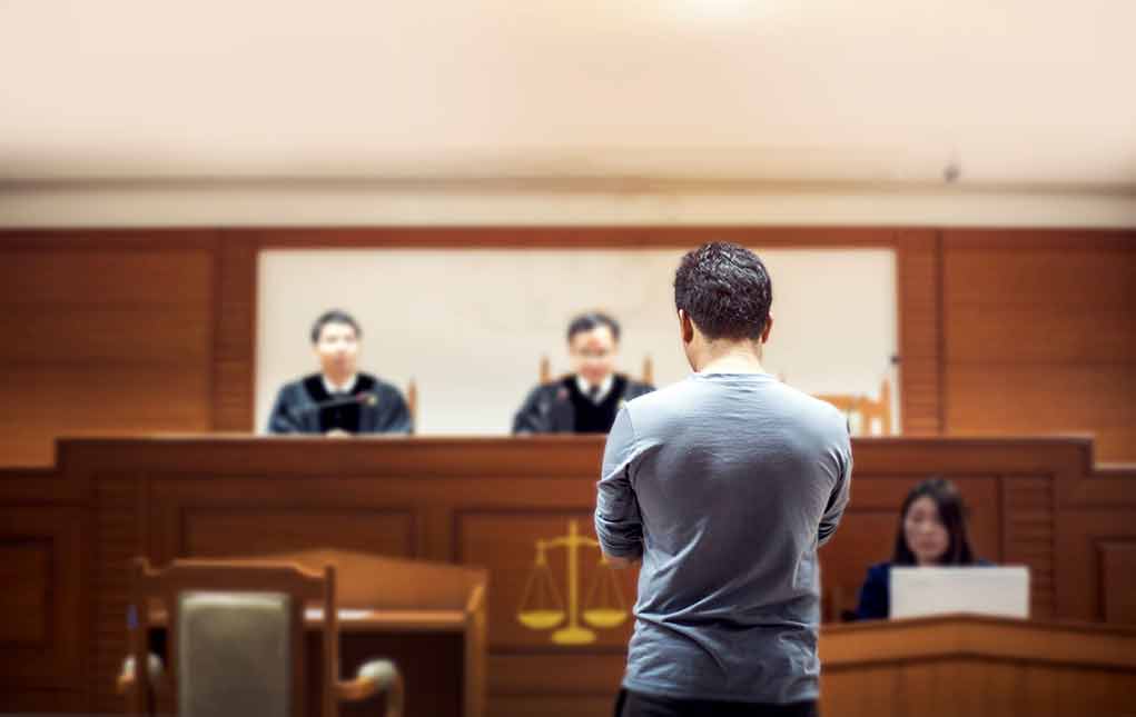Man stands in courtroom before judges and stenographer