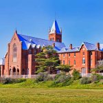 MIT ABANDONS DEI — Merit Rules Now Large red brick building with turrets and green lawn