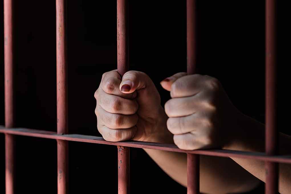592930874 featured image Hands gripping red jail bars tightly