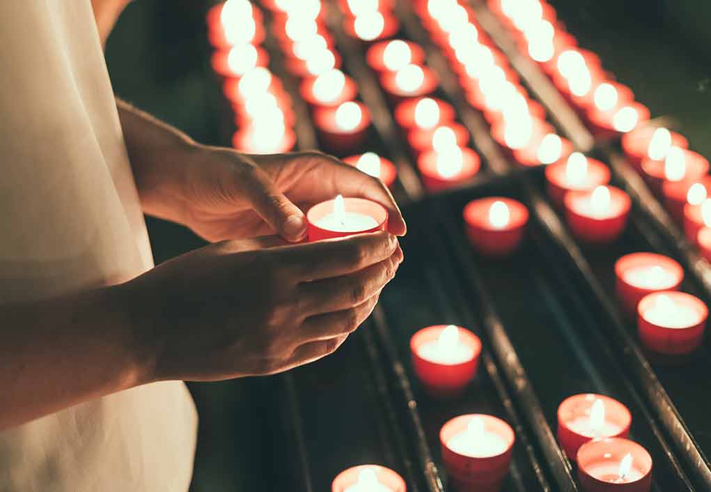 756377692 featured image Hands holding a candle near several lit candles.