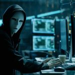 Media Giant HACKED — Sensitive Investigations Exposed Person wearing mask and hoodie at computer desk