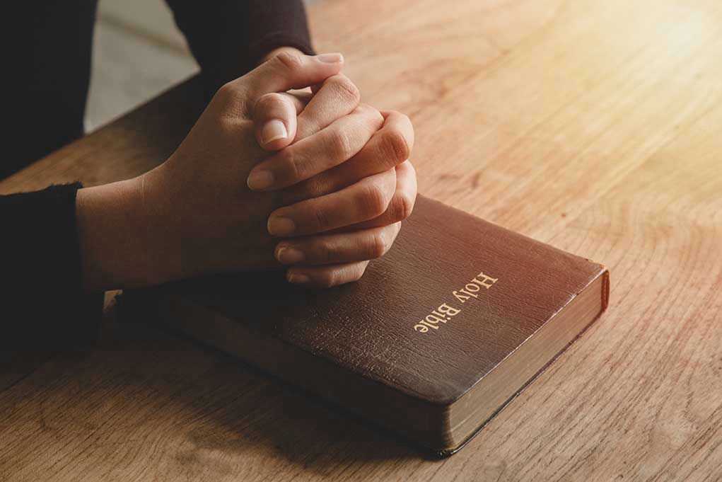 1801756960 Hands praying on a Bible
