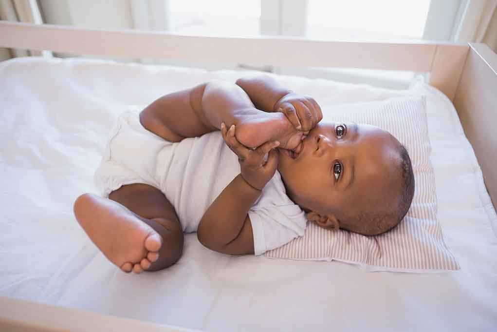 shutterstock_209676313.jpg A playful baby lying in a crib holding their feet