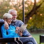 Older couple sitting on bench using tablet outdoors