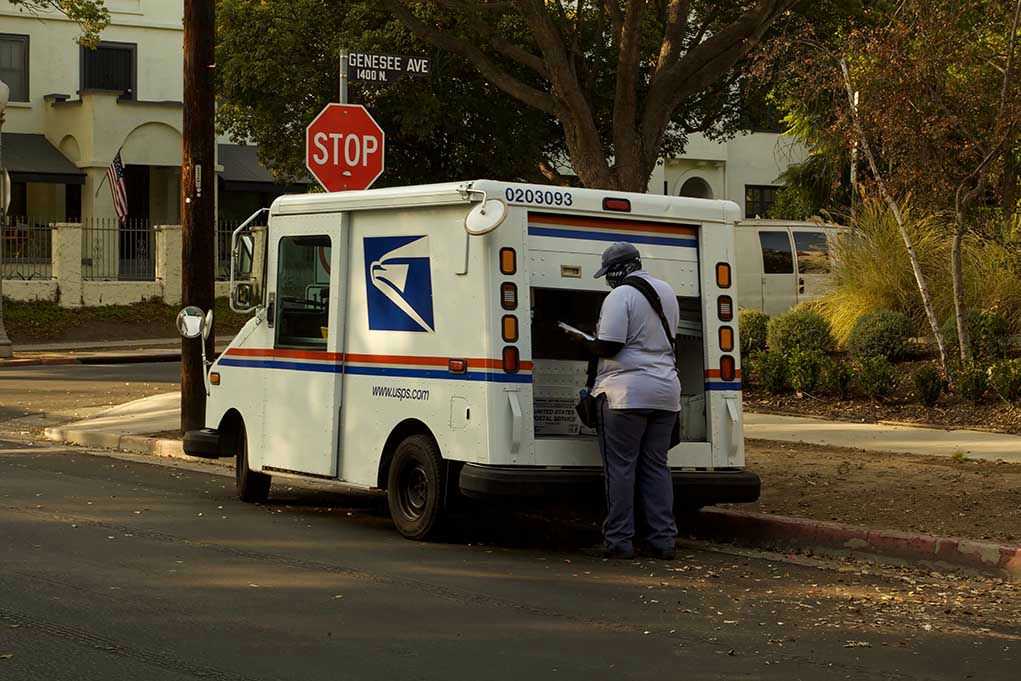 1862757586 USPS mail carrier at truck near stop sign.