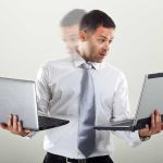 People Working More Hours But Achieving Less — What’s Behind It Man holding two laptops and looking surprised.