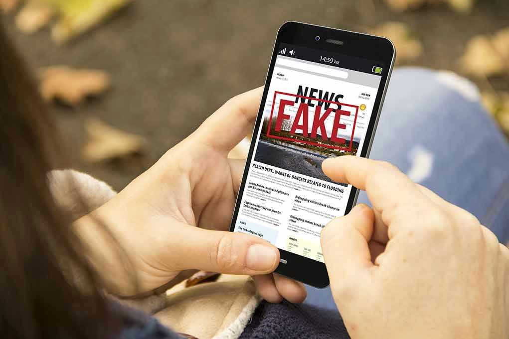 Person holding smartphone displaying fake news notification.