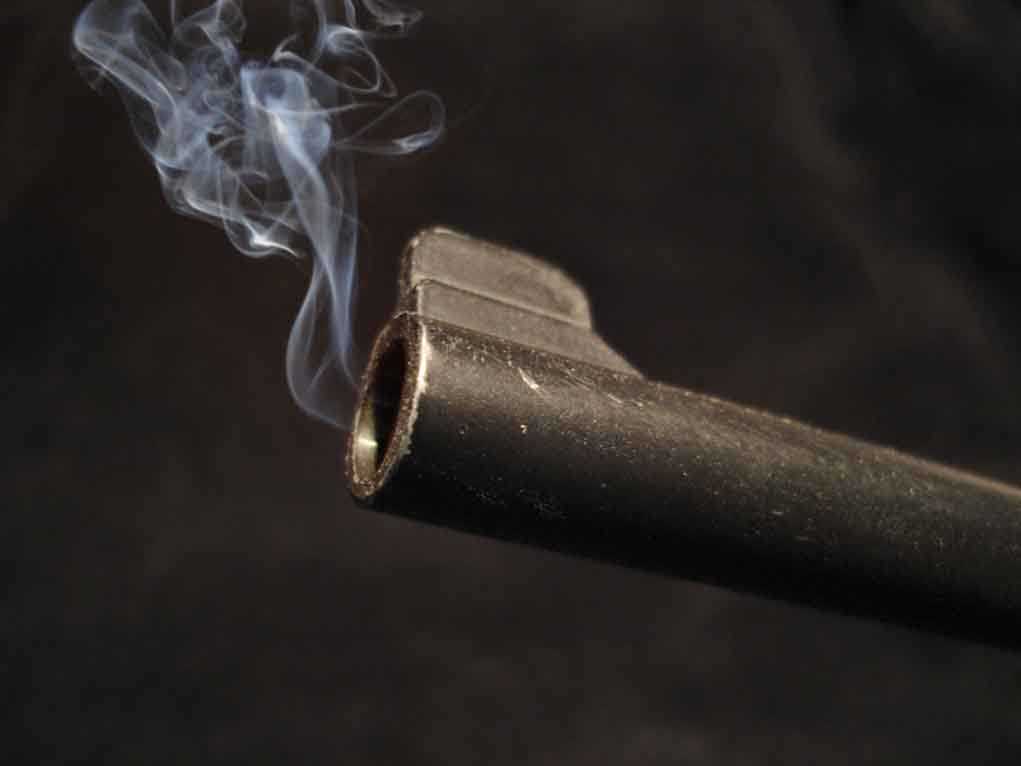 Close-up of a gun barrel emitting smoke against a black background