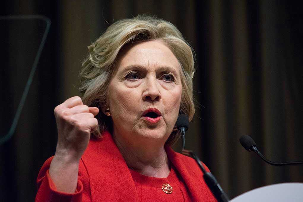 Person speaking passionately at a podium, wearing red jacket.