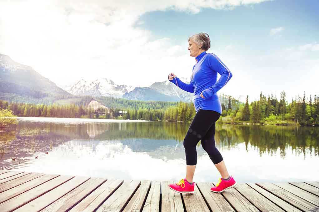 Senior woman jogging along a lakeside with mountains in the background