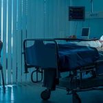 Health Dept SOUNDS ALARM- Cases Mounting! Woman sitting beside hospital bed at night.