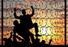 Silhouettes of people climbing barbed wire fence.