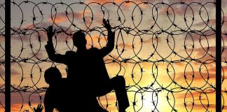 Silhouettes of people climbing barbed wire fence.