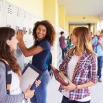 Teenage Deaths Surge—DEADLY TREND Gaining Popularity! Three high school students interacting near lockers in a hallway