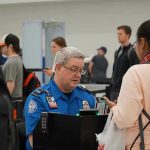 $10,000 Bonuses IGNITE Airport Uproar TSA agent checks passengers documents at airport security.