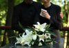 Mourners in black holding white flowers at funeral.