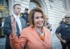 Pelosi’s 16,930% Return—How Is This Allowed? Woman in orange blazer speaking, surrounded by security personnel.