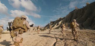 Soldiers running on rocky terrain with backpacks.
