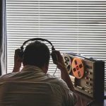 Russian Sex Spy Invasion Hits America’s ELITE Person listening to a vintage tape recorder with headphones