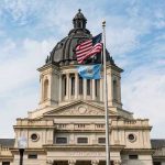 Building with dome and flags flying outside.