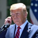 Trump Pardoned Convict ARRESTED AGAIN – Faces New Charges Man in a suit adjusting an earpiece.